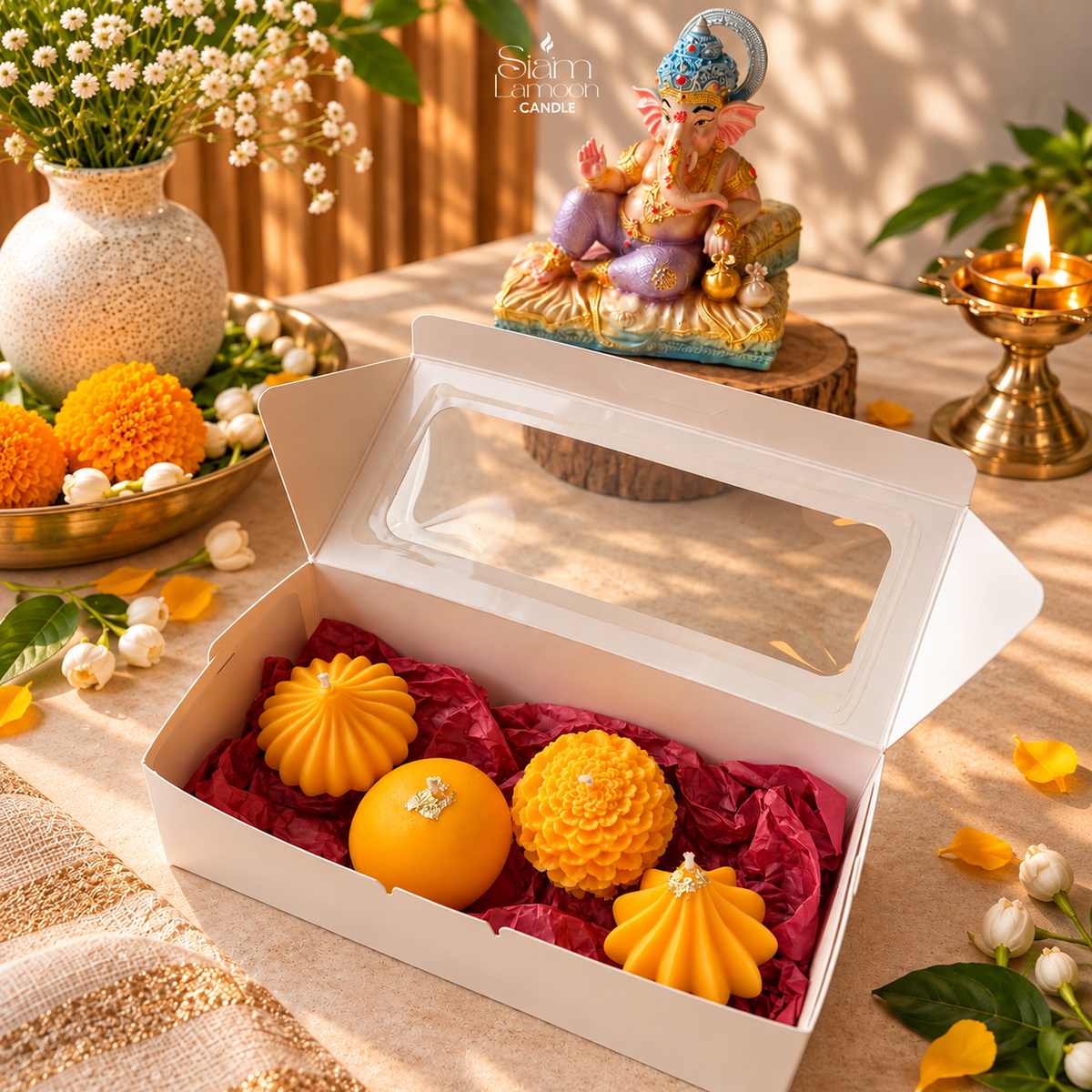 Open gift box holding four sculpted candles on a table with marigolds and a brass lamp